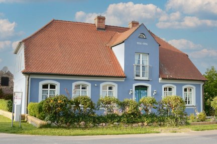 zeigt blau angestrichenes Haus mit weiß in Stuck abgesetzten Fenstern und Tür sowie rotem Ziegeldach